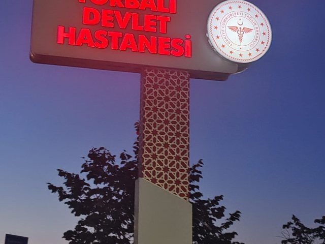 Torbalı Devlet Hastanesi ışıklı totem tabela; kırmızı harfler ve amblemli yuvarlak ışıklı kutu