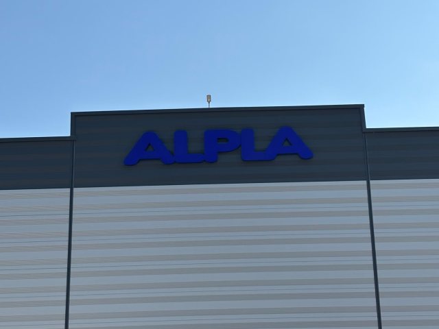 ALPLA fabrika cephesinde mavi kutu harf tabela; sağda sepetli vinç